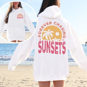 a woman standing on a beach wearing a white sweatshirt