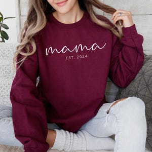 a woman sitting on a couch wearing a maroon sweatshirt
