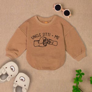 May include: Tan long-sleeve sweatshirt with a black graphic of two fists bumping. The text "UNCLE SITTI + ME" is above the fists.