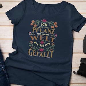 Pode incluir: Uma camiseta azul marinho com um design floral e o texto "Ich pflanz mir meine Welt wie sie mir gefällt".