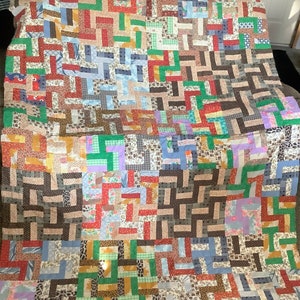 May include: A large patchwork quilt with a variety of colors and patterns, including brown, green, blue, red, and white. The quilt is made up of squares and rectangles, and the patterns are arranged in a geometric design.