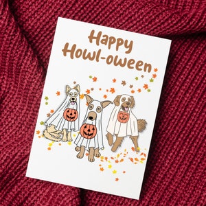 May include: A white card with the text "Happy Howl-oween" in brown lettering. Three cartoon dogs dressed as ghosts are holding pumpkins. The dogs are on a white background with scattered orange and yellow leaves.