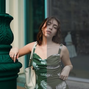 May include: A woman wearing a green and white tropical print dress with a white handbag. She is standing in front of a building with large windows.
