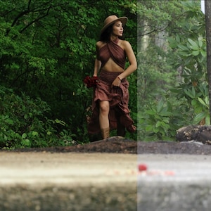 May include: A woman in a brown halter top and skirt walks through a lush green forest. She is wearing a wide-brimmed hat and carrying a bouquet of red flowers.