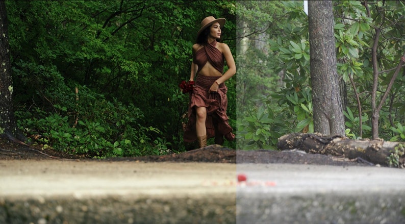 May include: A woman in a brown halter top and skirt walks through a lush green forest. She is wearing a wide-brimmed hat and carrying a bouquet of red flowers.