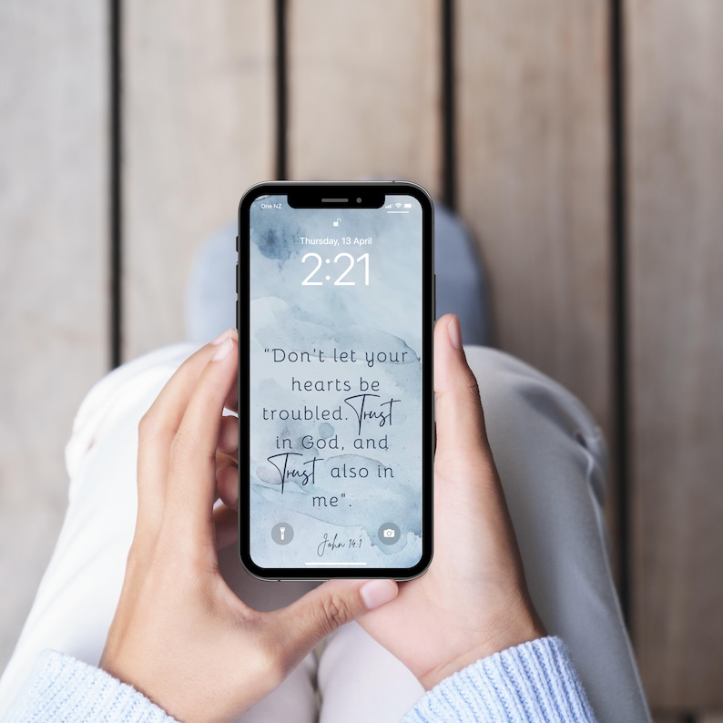 Pu&ograve; includere: Uno smartphone che mostra una schermata di blocco con una citazione dalla Bibbia: "Non si turbi il vostro cuore. Abbiate fede in Dio e abbiate fede anche in me." La citazione &egrave; tratta da Giovanni 14:1. Lo sfondo &egrave; un design ad acquerello in tonalit&agrave; blu.