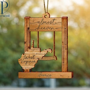 May include: A wooden hanging ornament featuring a cutout of the state of West Virginia. The design includes the text "almost heaven" at the top, "West Virginia" on the state shape, and "Jessica 2026" engraved on the bottom horizontal bar.