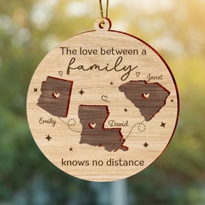 May include: Wooden family ornament with three state cutouts, connected by dotted lines. The ornament features the text "The love between a family knows no distance" and names "Emily," "David," and "Janet."
