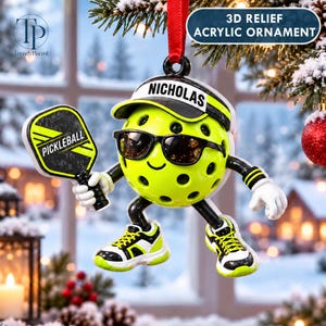 May include: A 3D relief acrylic ornament shaped like a yellow pickleball with a face, wearing black sunglasses and a visor with the name NICHOLAS printed on it. The character holds a black and yellow pickleball paddle and wears trainers.