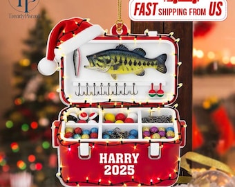 May include: A red tackle box ornament featuring a Santa hat on top and string lights wrapped around the frame. The interior displays a bass fish, hooks, and colorful fishing lures. The front is printed with the text HARRY 2025 in white letters.