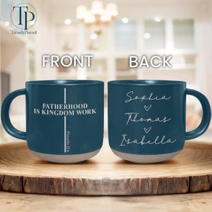May include: A teal ceramic mug with a gray base. The front of the mug reads "FATHERHOOD IS KINGDOM WORK" with "Proverbs 22:6" below. The back of the mug has the names "Sophia", "Thomas", and "Isabella".