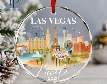 May include: A circular glass ornament featuring a colorful Las Vegas skyline illustration, including the Eiffel Tower, a Ferris wheel, and the Welcome to Fabulous Las Vegas sign. The text reads LAS VEGAS, Nicole, and 2026, suspended by a red ribbon.