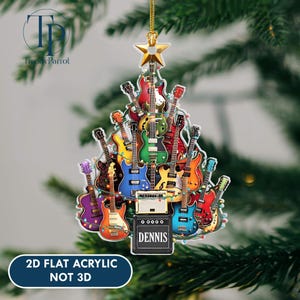 May include: A colorful Christmas tree ornament shaped like a guitar. The ornament is made of acrylic and features a variety of guitars in different colors, with a gold star at the top. The text "DENNIS" is on the bottom. The text "2D FLAT ACRYLIC NOT 3D" is also visible.