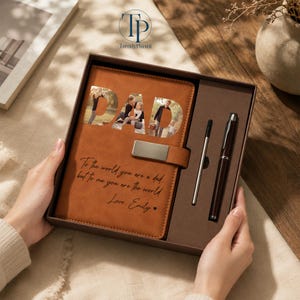 K&ouml;nnte beinhalten: Ein braunes Lederjournal mit dem Wort "DAD" ausgeschnitten, um Familienfotos freizugeben. Das Journal enth&auml;lt einen Stift und einen Bleistift sowie die Inschrift "To the world you are a dad, but to me you are the world. Love, Emily."