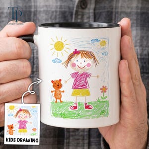 May include: White ceramic mug with a black interior and handle, featuring a colorful child's drawing. The drawing depicts a girl in a pink shirt and yellow shorts, a sun, clouds, and a flower. The words "KIDS DRAWING" are on a small image.
