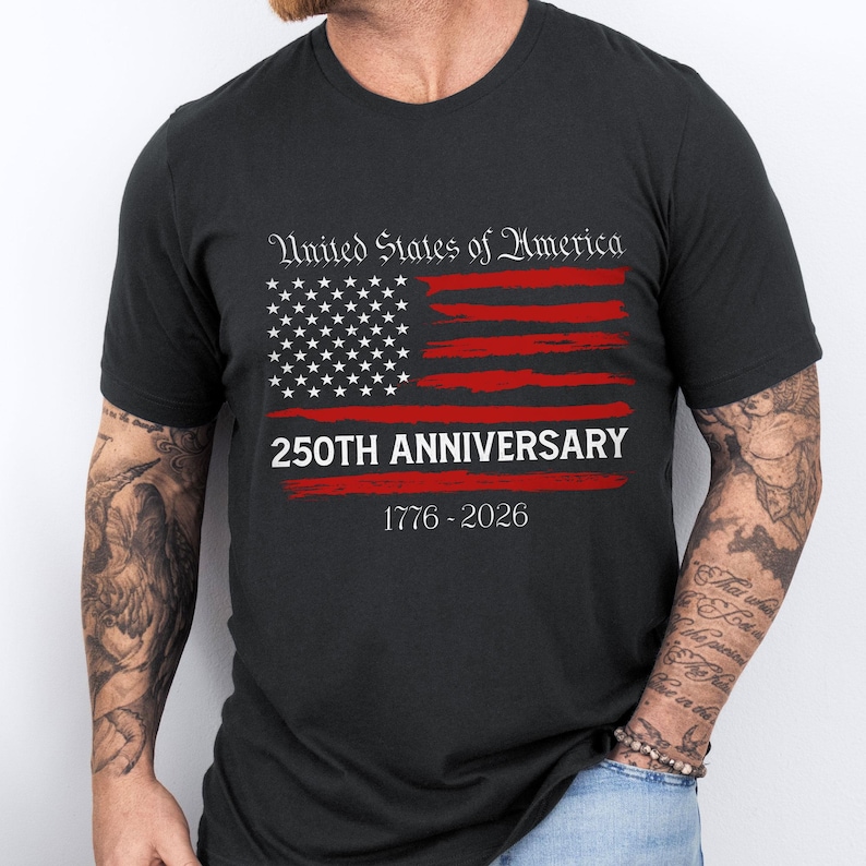 May include: Black t-shirt featuring a distressed American flag design in red and white. The text "United States of America" is above the flag, with "250TH ANNIVERSARY" and "1776-2026" below. A patriotic design for a special occasion.