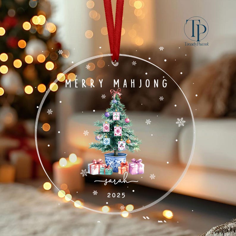 May include: Clear Christmas ornament with a red ribbon. The ornament features a watercolor Christmas tree with mahjong tiles, gifts, and the text "MERRY MAHJONG", "Sarah", and "2025". The ornament is round with snowflake accents.
