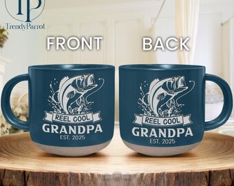 May include: Two ceramic mugs with a dark blue finish and a light gray base. Each mug features a white graphic of a leaping fish and the text "REEL COOL GRANDPA EST. 2025". The mugs are displayed on a wooden surface.