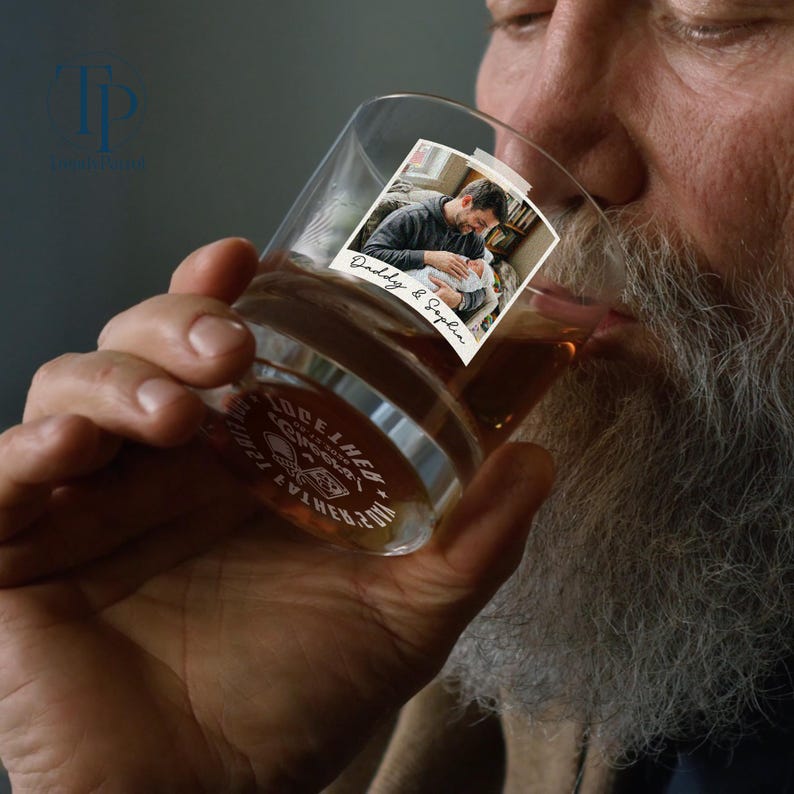 May include: A clear whiskey glass with a photo of a man holding a baby, labeled "Daddy & Sophia." The glass has a silver band with the words "TOGETHER" and "EST. 2017." The glass is filled with amber liquid.