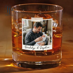 May include: A clear glass tumbler filled with ice and amber liquid. A photo of a man holding a baby is adhered to the glass. The photo has the words "Daddy & Sophia" written on it.