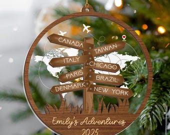May include: A wooden Christmas ornament with a signpost design. The signposts point to various locations, including Canada, Italy, and Taiwan. The ornament has the text "Emily's Adventures 2025".