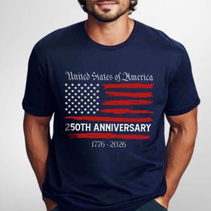 May include: Navy blue t-shirt with a distressed American flag design in red and white. The shirt features the text "United States of America" above the flag and "250th Anniversary 1776-2026" below it. A patriotic themed tee.