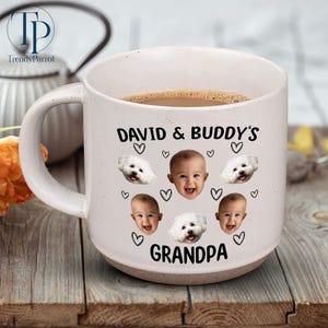 May include: White ceramic mug with a black handle. The mug has a black inscription that reads "David & Buddy's Grandpa". There are four images of a small white dog and three images of a baby's face on the mug.