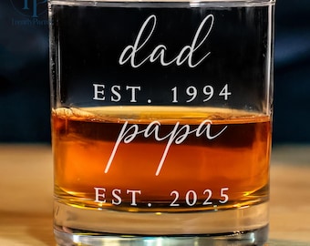 May include: A clear glass tumbler with the text "dad est. 1994 papa est. 2025" etched on the side. The glass is filled with amber liquid.