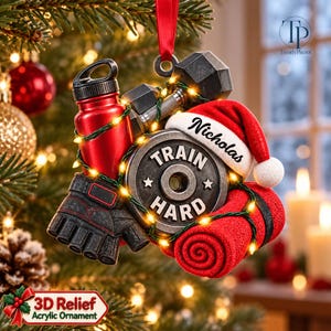 May include: A fitness-themed Christmas ornament featuring a red water bottle, a black dumbbell, a weight plate with the text TRAIN HARD, a pair of black workout gloves, and a red towel, all topped with a Santa hat personalized with the name Nicholas.