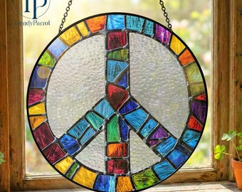 May include: A round stained glass peace sign with a black border, hanging from a chain. The peace symbol is filled with colorful glass pieces in shades of red, blue, green, orange, and yellow. The background is a window.