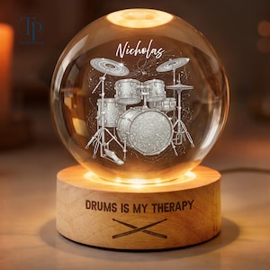 May include: A spherical glass lamp featuring an etched drum kit design and the name Nicholas. The light sits on a cylindrical wooden base engraved with the text DRUMS IS MY THERAPY and an illustration of two crossed drumsticks.