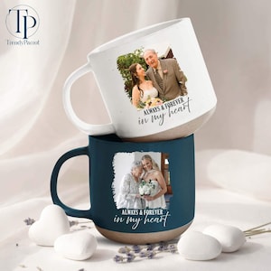 May include: Two ceramic mugs, one white and one navy blue, stacked. Each mug features a photograph and the text "ALWAYS & FOREVER in my heart." The white mug has a speckled finish, while the navy mug has a solid color. Both mugs have a beige base.