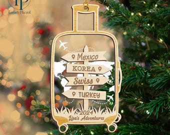 May include: Wooden Christmas ornament shaped like a suitcase with a world map and directional signs pointing to Mexico, Korea, Swiss, and Turkey. The ornament also includes the text "2024 Lisa's Adventures".