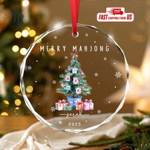 May include: A clear, round Christmas ornament with a red ribbon. The ornament features a Christmas tree decorated with Mahjong tiles, gifts, and the text "MERRY MAHJONG" and "Sarah 2025".