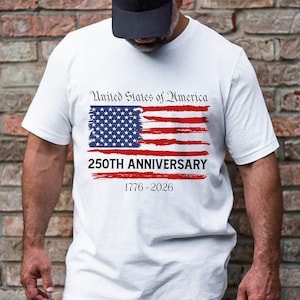 May include: White t-shirt featuring a distressed American flag design with the text "United States of America" above and "250TH ANNIVERSARY 1776-2026" below. The flag has a blue field of stars and red stripes.