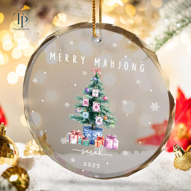 May include: A clear, round Christmas ornament with the text "MERRY MAHJONG" and a watercolor Christmas tree decorated with Mahjong tiles. The ornament also features the name "Sarah" and the year "2025".