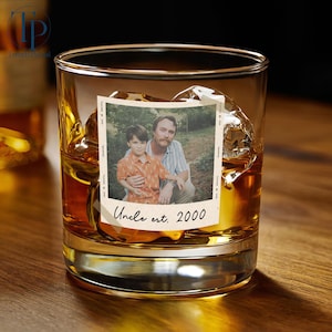 May include: A rocks glass filled with amber liquid and ice cubes, featuring a photo with a man and a child. The photo has the text "Uncle est. 2000" at the bottom. The glass sits on a wooden surface.