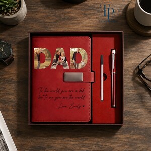 K&ouml;nnte beinhalten: Ein rotes Leder-Notizbuch-Set mit einem Stift und einem Kugelschreiber. Das Notizbuch hat das Wort "DAD" ausgeschnitten, das Fotos zeigt. Das Notizbuch hat auch den Text "To the world you are a dad, but to me you are the world. Love, Emily."