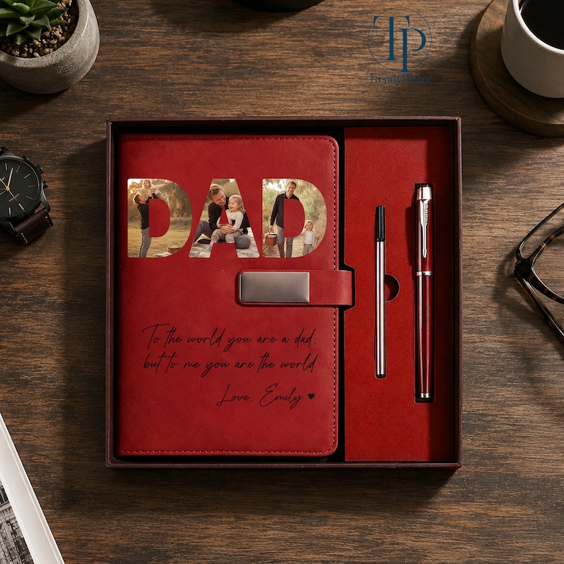K&ouml;nnte beinhalten: Ein rotes Leder-Notizbuch-Set mit einem Stift und einem Kugelschreiber. Das Notizbuch hat das Wort "DAD" ausgeschnitten, das Fotos zeigt. Das Notizbuch hat auch den Text "To the world you are a dad, but to me you are the world. Love, Emily."