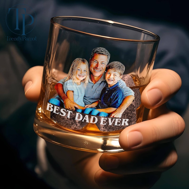 May include: A clear, personalized whiskey glass with a family photo and the text "BEST DAD EVER." The image features a man and two children. The glass is held in a person's hand.