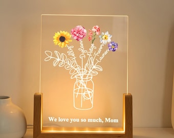 May include: A lighted acrylic panel with a floral design in a wooden base. The panel features a vase of flowers with a sunflower, pink, and purple blooms. Text at the bottom reads, "We love you so much, Mom."