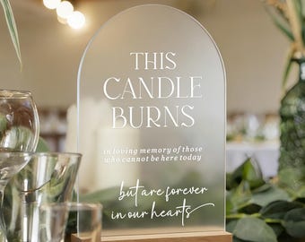 Könnte beinhalten: Ein bogenförmiges, mattiertes Acrylschild mit Holzsockel und dem weißen Text: THIS CANDLE BURNS in loving memory of those who cannot be here today but are forever in our hearts. Das Schild steht auf einem Tisch neben verschiedenen Gläsern.