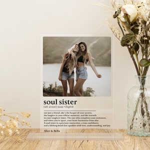 Könnte beinhalten: Ein weißer Acryl-Bilderrahmen mit einem Foto von zwei Frauen, die lächeln und gemeinsam im Freien stehen. Der Rahmen enthält eine Schwarzweißdefinition des Wortes "soul sister" mit dem Text "Alice & Bella" unten.