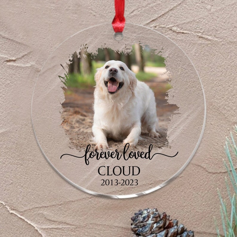 May include: A round, clear glass ornament with a photo of a white dog. The ornament has the text "forever loved CLOUD 2013-2023" printed on it.