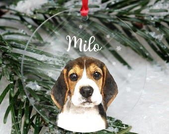 May include: A clear round Christmas ornament with a watercolor illustration of a Beagle puppy with brown and white fur. The ornament has a red ribbon and the name "Milo" printed on it.