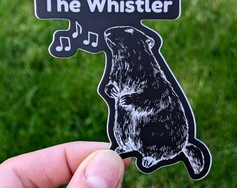 May include: Black and white sticker of a whistling marmot with musical notes above it. The sticker says "The Whistler" at the top.