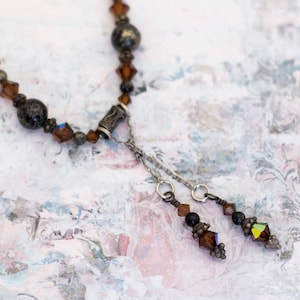 May include: A vintage necklace featuring a Y-shaped design with a mix of dark brown and silver-toned beads. The necklace has a central pendant with dangling accents, including faceted crystals and small beads. The overall aesthetic is antique and elegant.