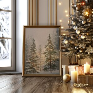 Puede incluir: Una impresi&oacute;n art&iacute;stica enmarcada de un bosque invernal con un marco dorado, apoyada en un suelo de madera. Un &aacute;rbol de Navidad decorado con adornos y luces est&aacute; en el fondo. Velas encendidas y regalos envueltos crean una escena festiva.