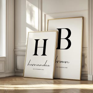 May include: Two framed art prints with gold trim. One features a large black letter "H" with the name "hernandez" and the date "EST. NOVEMBER 01, 2024". The other has a large black "B", the name "brown" and the date "EST. MARCH 08, 2022".