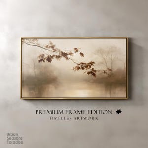 Op de afbeelding: Een rechthoekig landschapsschilderij in een dunne gouden lijst met een mistig, sepia-kleurig boslandschap en een opvallende tak met bruine herfstbladeren op de voorgrond. De tekst eronder luidt PREMIUM FRAME EDITION, TIMELESS ARTWORK.